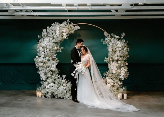 A couple showcasing minimalist elegance in front of a floral wedding arch.